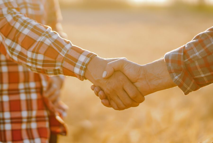 Two farmers shaking hands in a field, symbolising trusted partnerships in agriculture across New Zealand and Australia