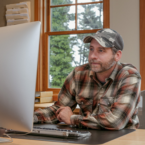 Dairy farmer using desktop computer to manage payroll and timesheets for farm staff in New Zealand